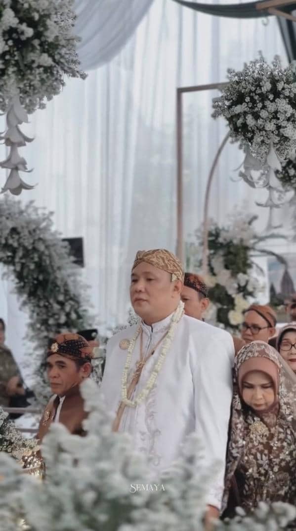 Wancoy Grind Boys berpose dalam potret pernikahan bersama pasangannya di depan dekorasi acara resmi.