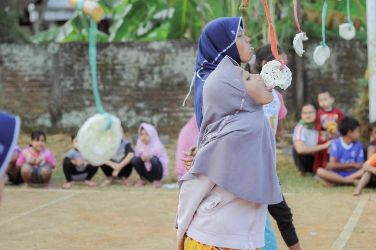 Ilustrasi peserta lomba makan kerupuk berusaha menghabiskan kerupuk yang digantung dalam perayaan kemerdekaan.