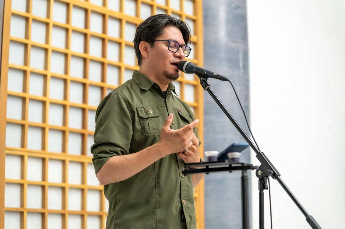 Ilustrasi seseorang berbicara di depan audiens dalam sesi presentasi di sebuah ruangan yang terang.