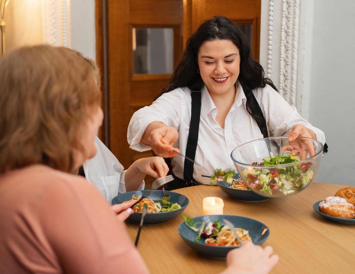 Sekelompok perempuan duduk bersama di meja makan, menikmati hidangan dalam ilustrasi momen mentraktir keluarga.