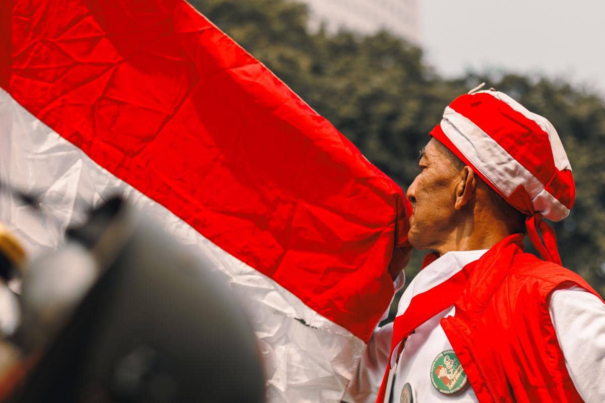 Seorang pria mengenakan pakaian merah putih memegang bendera Merah Putih