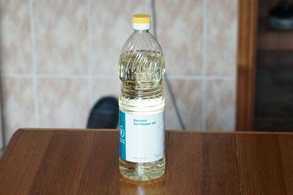 Botol minyak bunga matahari diletakkan di antara bunga matahari kuning sebagai ilustrasi minyak nabati.