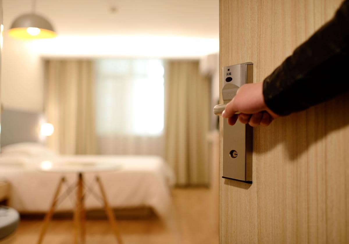 Kamar tidur bernuansa putih dengan tempat tidur rapi, lampu di sisi ranjang, dan jendela besar bercahaya.