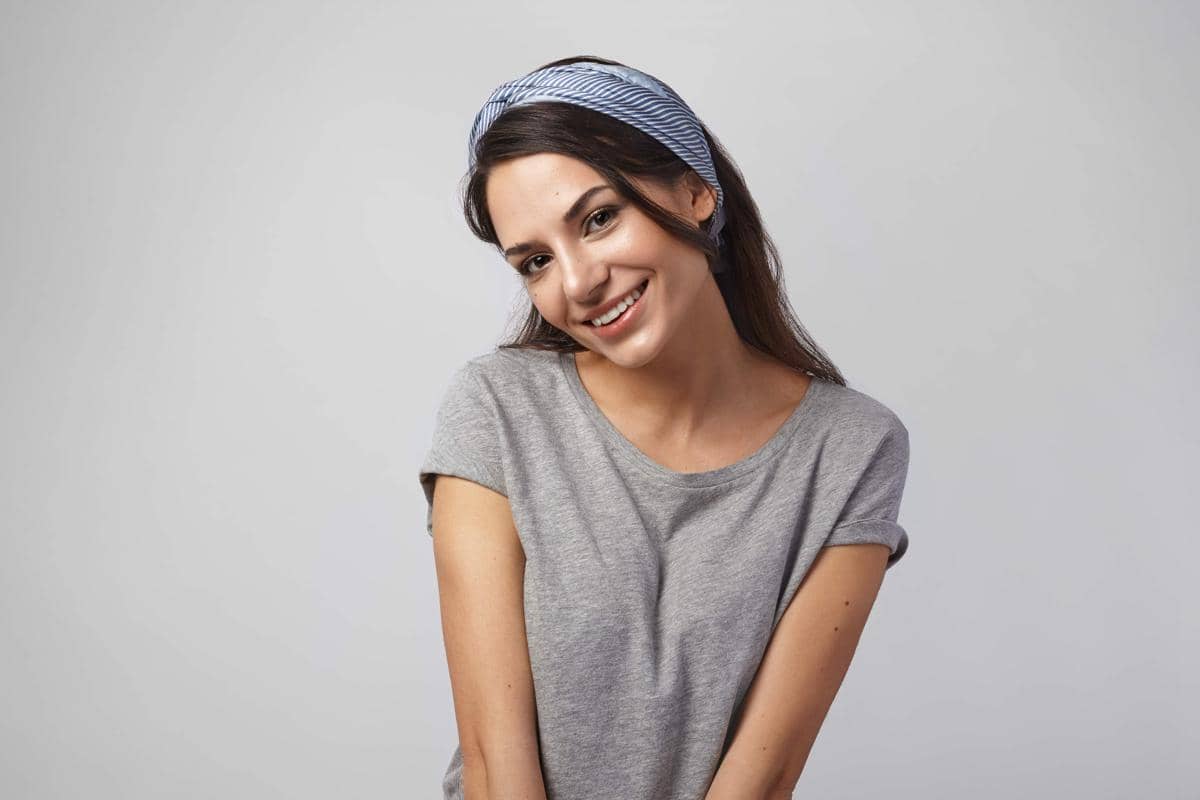 Seorang perempuan berambut panjang mengenakan aksesori rambut dan berpose ekspresif di studio dengan latar polos.