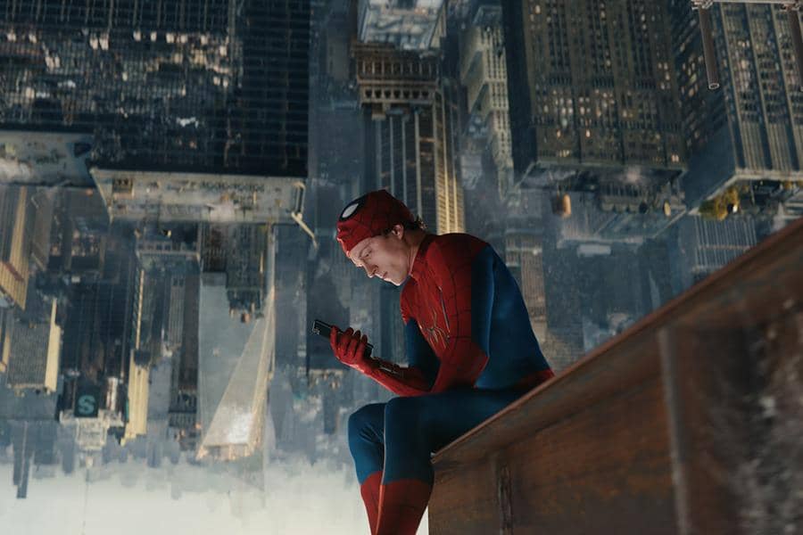 Spider-Man duduk di tepi gedung dengan kota terlihat terbalik di belakangnya