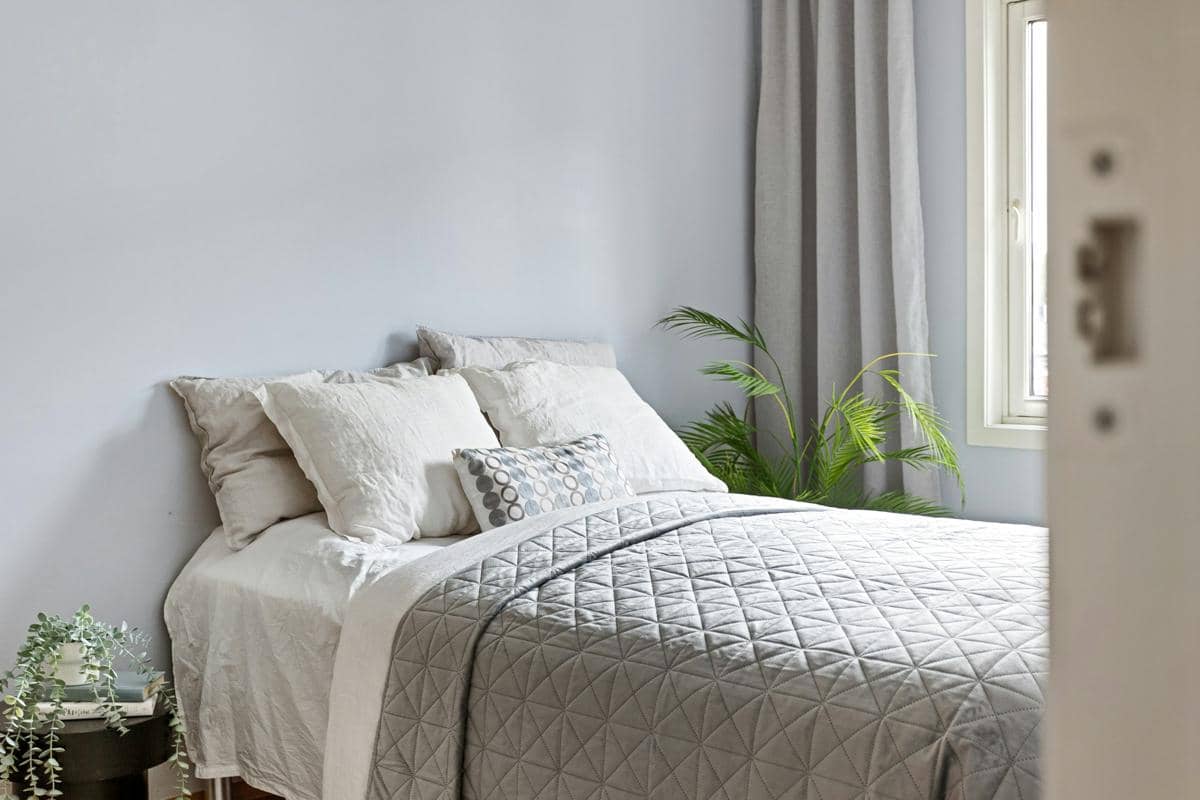 Tempat tidur bernuansa putih dengan sprai dan sarung bantal, menggambarkan perlengkapan tidur yang adem.