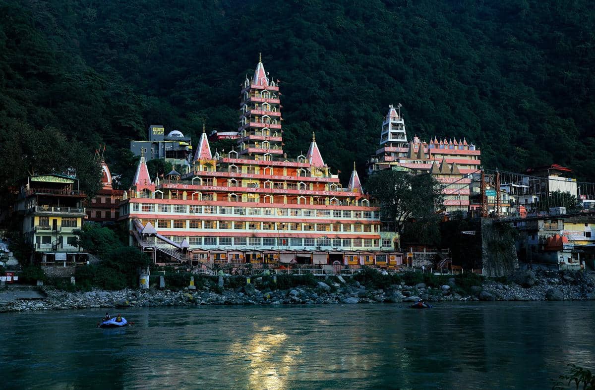 Fasad Kuil Tera Manzil berwarna-warni di Rishikesh dengan deretan balkon dan kubah kecil di bawah langit cerah.