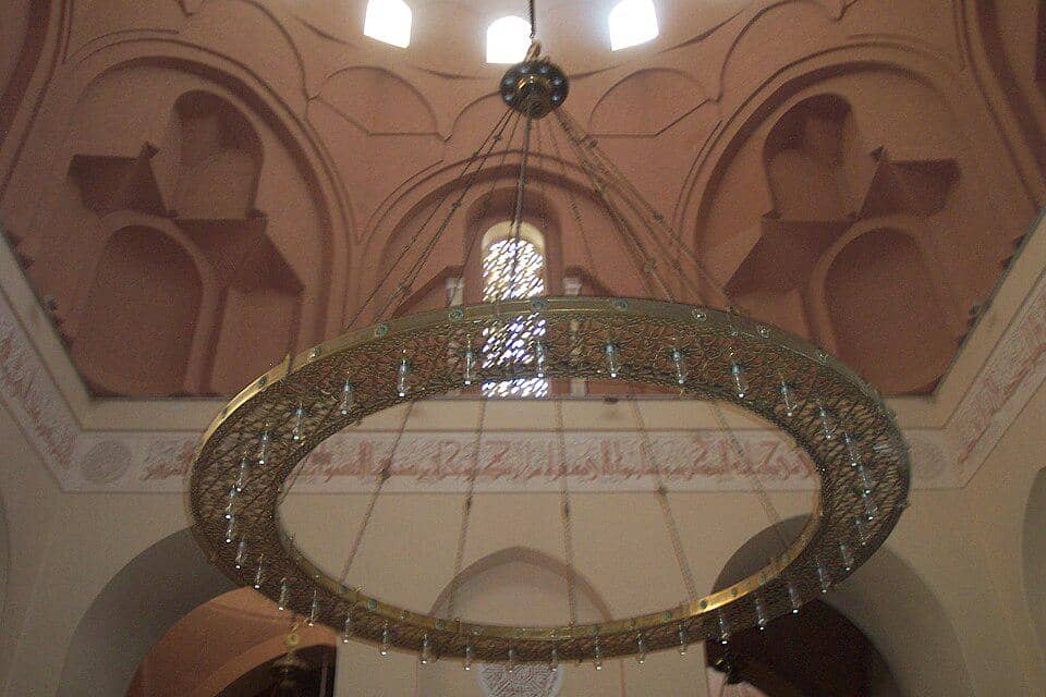 Lampu gantung di bagian dalam Masjid Raja Saud, difoto dalam sudut pandang vertikal yang menonjolkan pencahayaan.