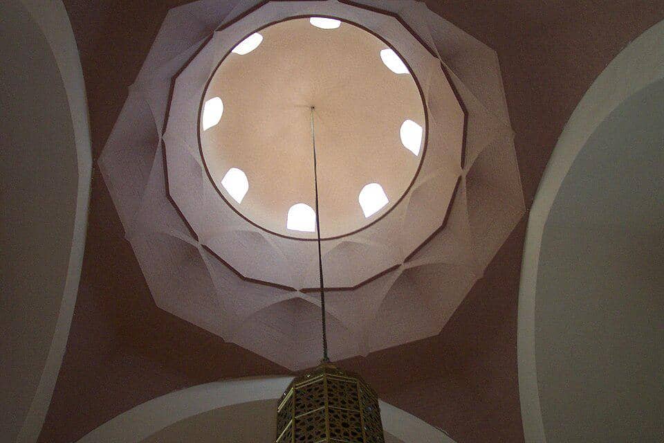 Detail bagian dalam kubah Masjid Raja Saud dengan hiasan geometris dan kaligrafi bernuansa biru, emas, serta putih.