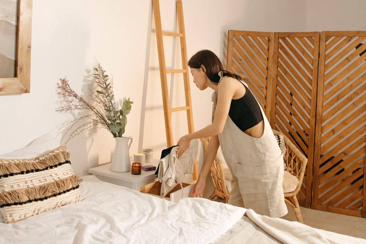 Meja samping kasur kayu di kamar tidur dengan lampu, buku, dan dekorasi minimalis yang tersusun rapi di atasnya.
