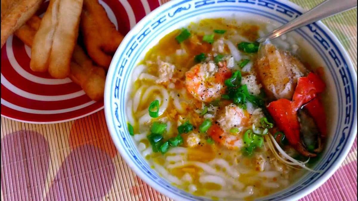 Ilustrasi banh canh cua, sajian mi Vietnam dalam kuah kental dengan kepiting dan aneka pelengkap di mangkuk.