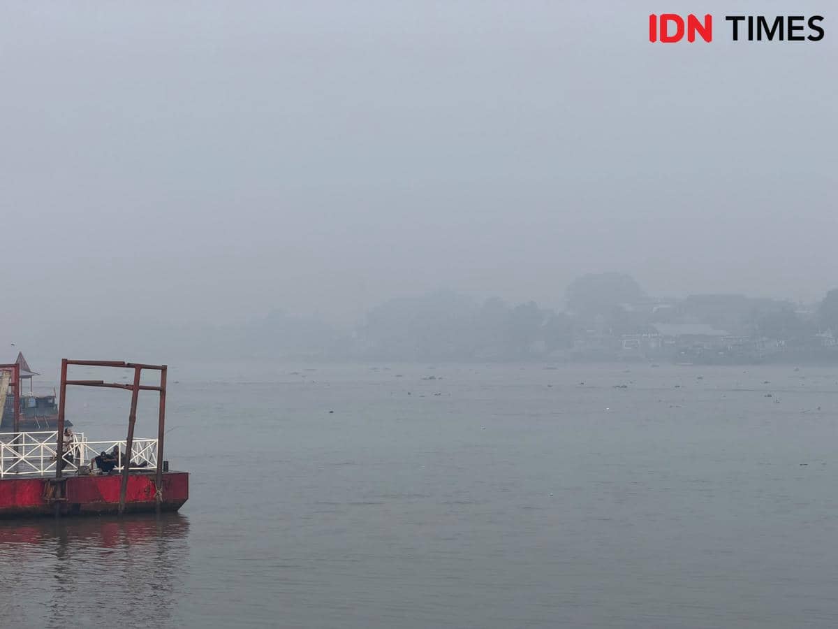 Perairan Sungai Musi di Palembang tampak tertutup kabut asap, dengan pandangan di atas sungai yang memudar.