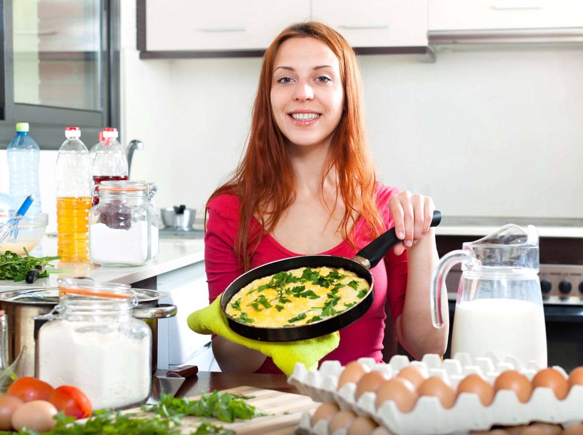 Seorang perempuan memasak telur orak-arik di wajan di dapur rumah sebagai ilustrasi persiapan telur dadar.