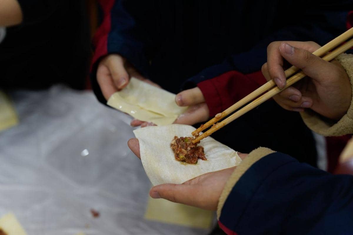 Tangan menambahkan isian ayam ke lembaran kulit pangsit di atas meja sebagai persiapan membuat pangsit.