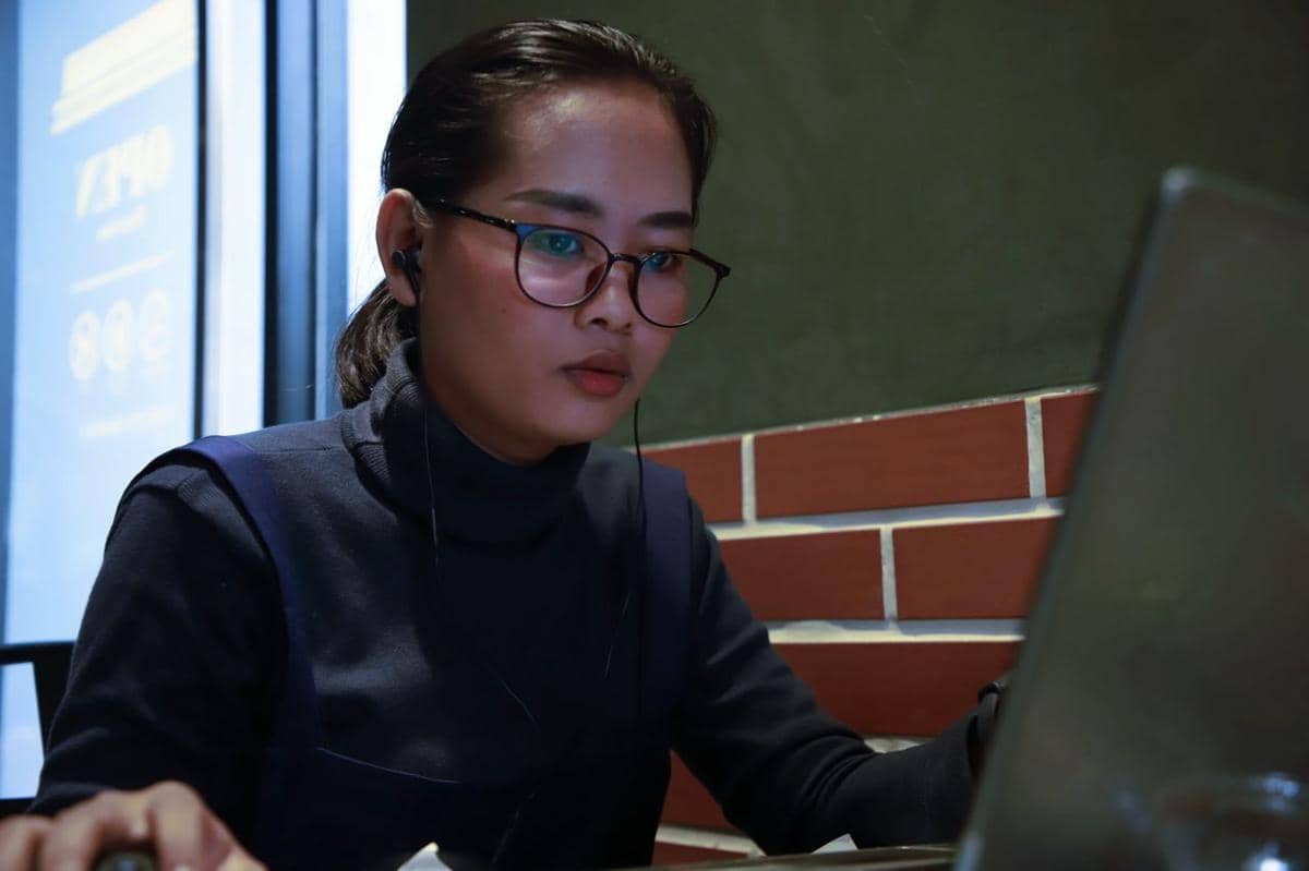 Ilustrasi seseorang bekerja dengan laptop di meja, menggambarkan aktivitas profesional dalam suasana kerja modern.