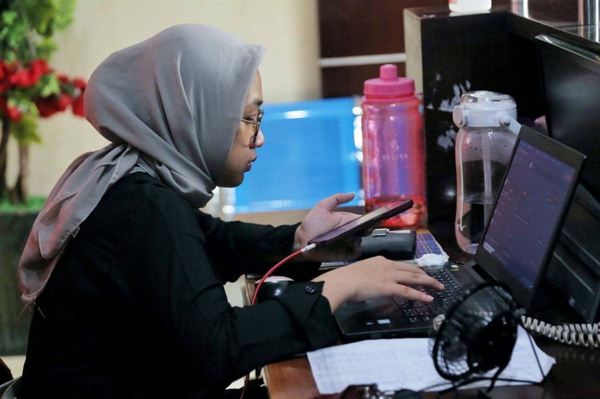 Ilustrasi suasana bekerja dengan seseorang menggunakan laptop di meja dalam ruangan yang terang dan rapi.