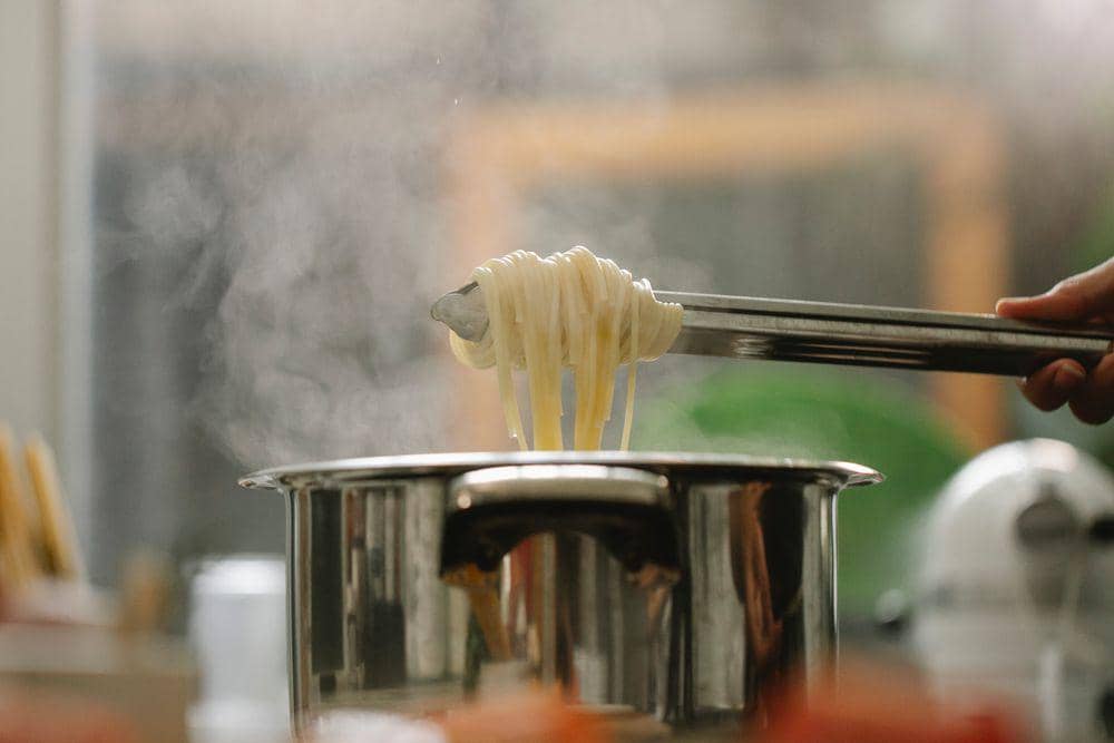 Panci berisi mi sedang direbus di atas kompor sebagai ilustrasi proses memasak mi di dapur rumah sederhana.