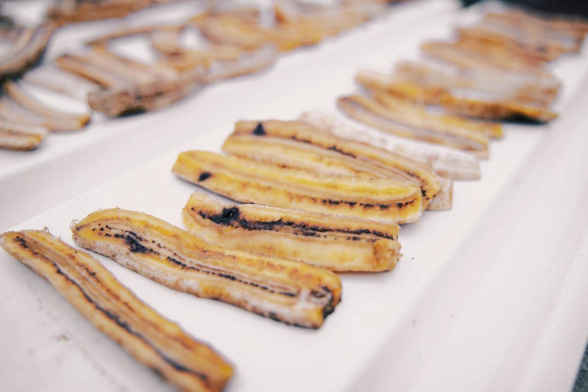 Irisan pisang matang tersusun di atas permukaan putih, memperlihatkan tekstur lembut dan warna kuning pucat.
