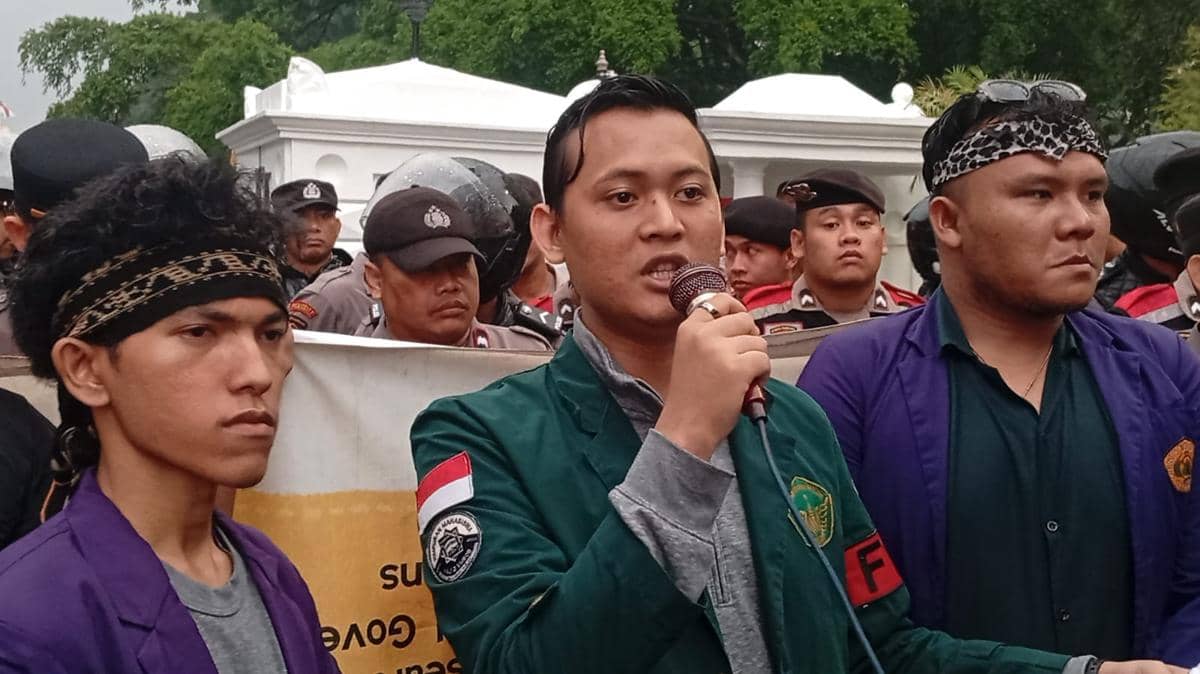 Seorang mahasiswa berorasi menyampaikan aspirasi di hadapan aparat yang berjaga dalam sebuah aksi mahasiswa.