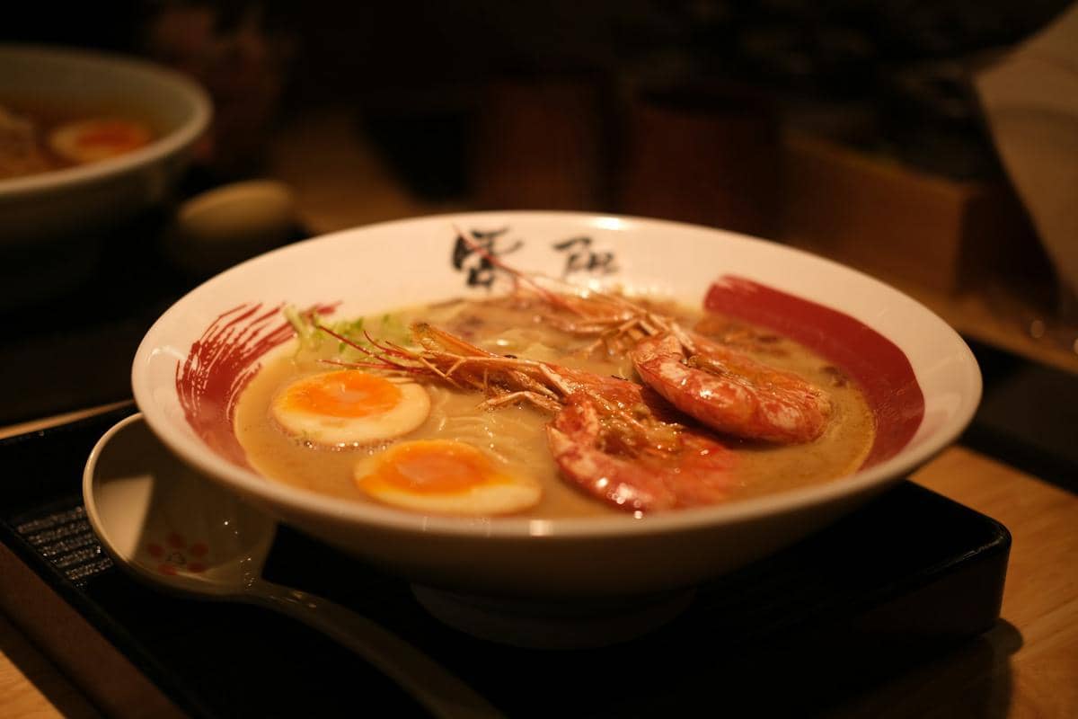 Ilustrasi semangkuk creamy tom yum udon, hidangan mi berkuah kental dengan warna hangat yang menggugah selera.