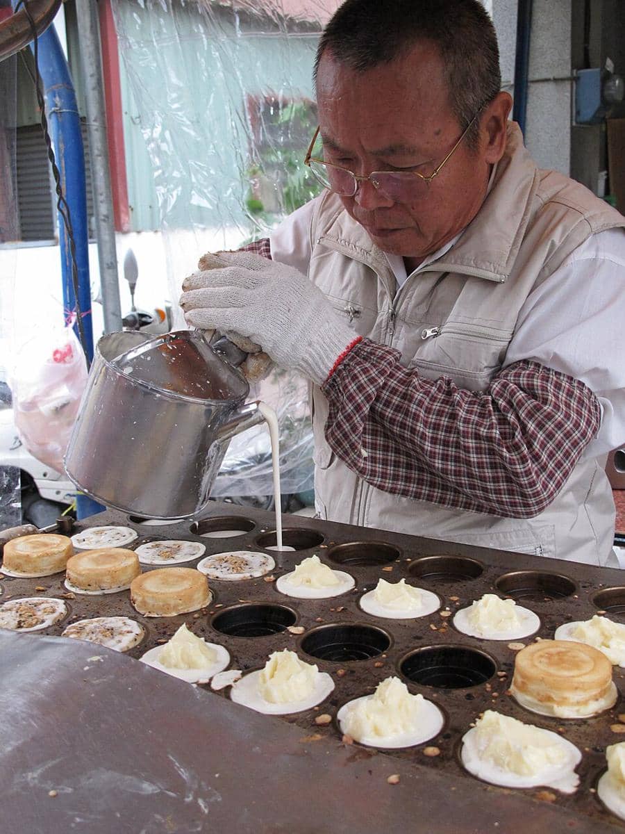 Ilustrasi pedagang menyiapkan obanyaki, kue bulat panggang berisi aneka isian, di atas cetakan khusus.