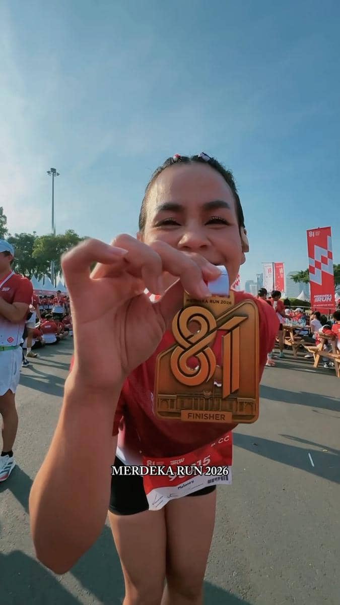 Seorang artis berpose mengenakan kaus olahraga hitam dan medali usai mengikuti acara Merdeka Run 2026.