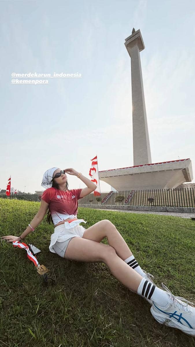 Artis peserta Merdeka Run 2026 berpose mengenakan kaus acara di area kegiatan lari bersama peserta lain.