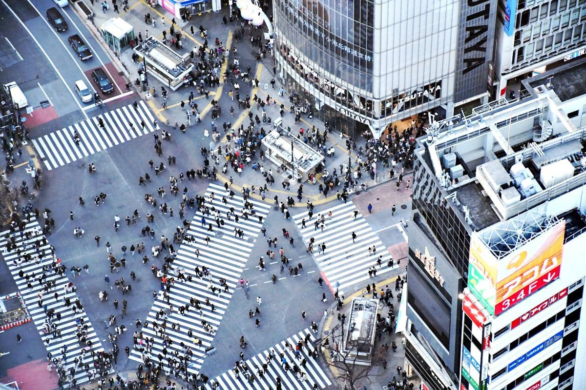 Kerumunan pejalan kaki melintasi Shibuya Crossing di Tokyo, Jepang, dikelilingi jalan raya dan gedung-gedung perkotaan.