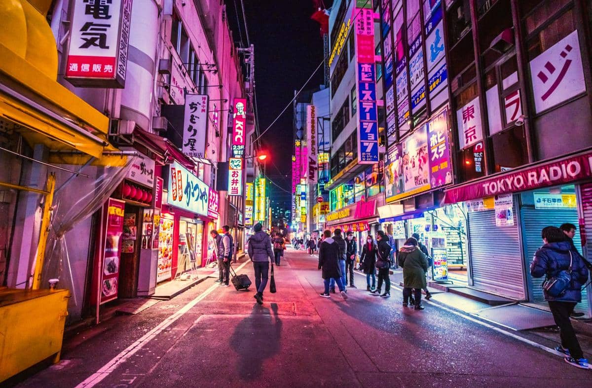 Deretan gedung bertingkat dengan papan iklan dan lampu neon di kawasan Akihabara, Jepang, di tepi jalan kota.