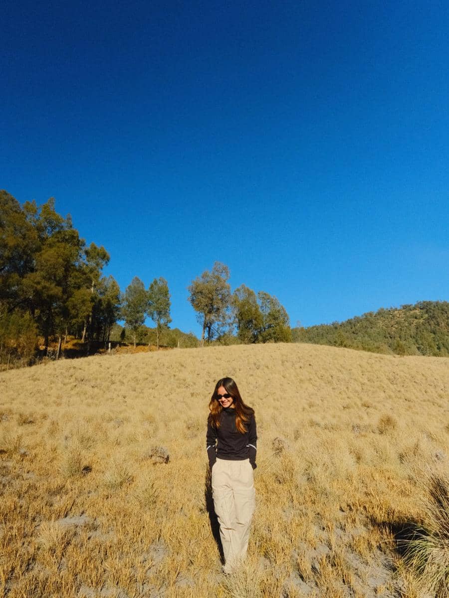 Bella Graceva berjalan di jalur Cemoro Kandang, kawasan pendakian Gunung Semeru, dengan latar pepohonan dan medan alam.