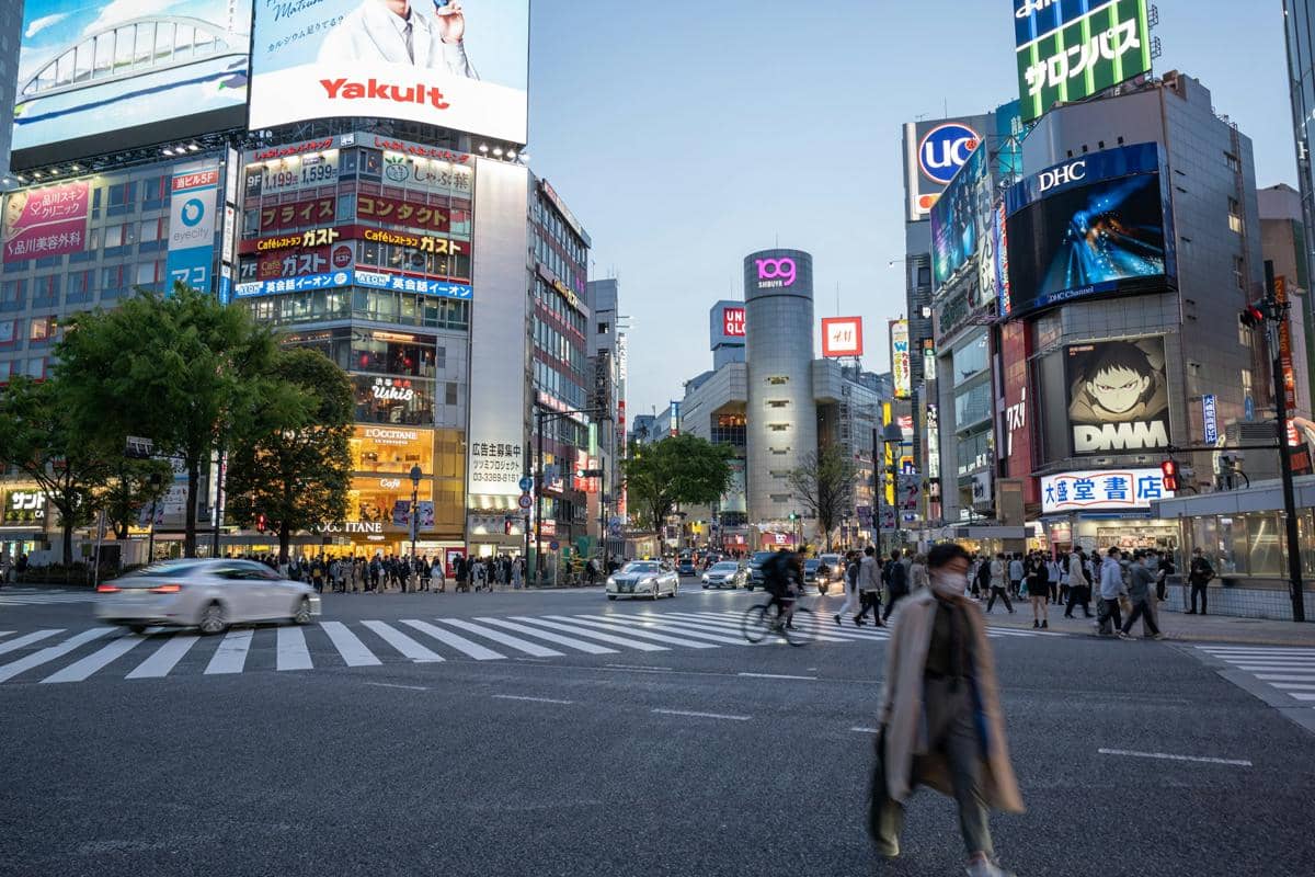 Kerumunan pejalan kaki melintasi zebra cross di Shibuya Crossing, Tokyo, Jepang, di antara gedung dan reklame kota.