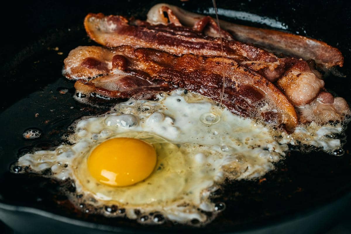 Ilustrasi memasak daging dan telur di atas wajan, menggambarkan persiapan hidangan rumahan sederhana.