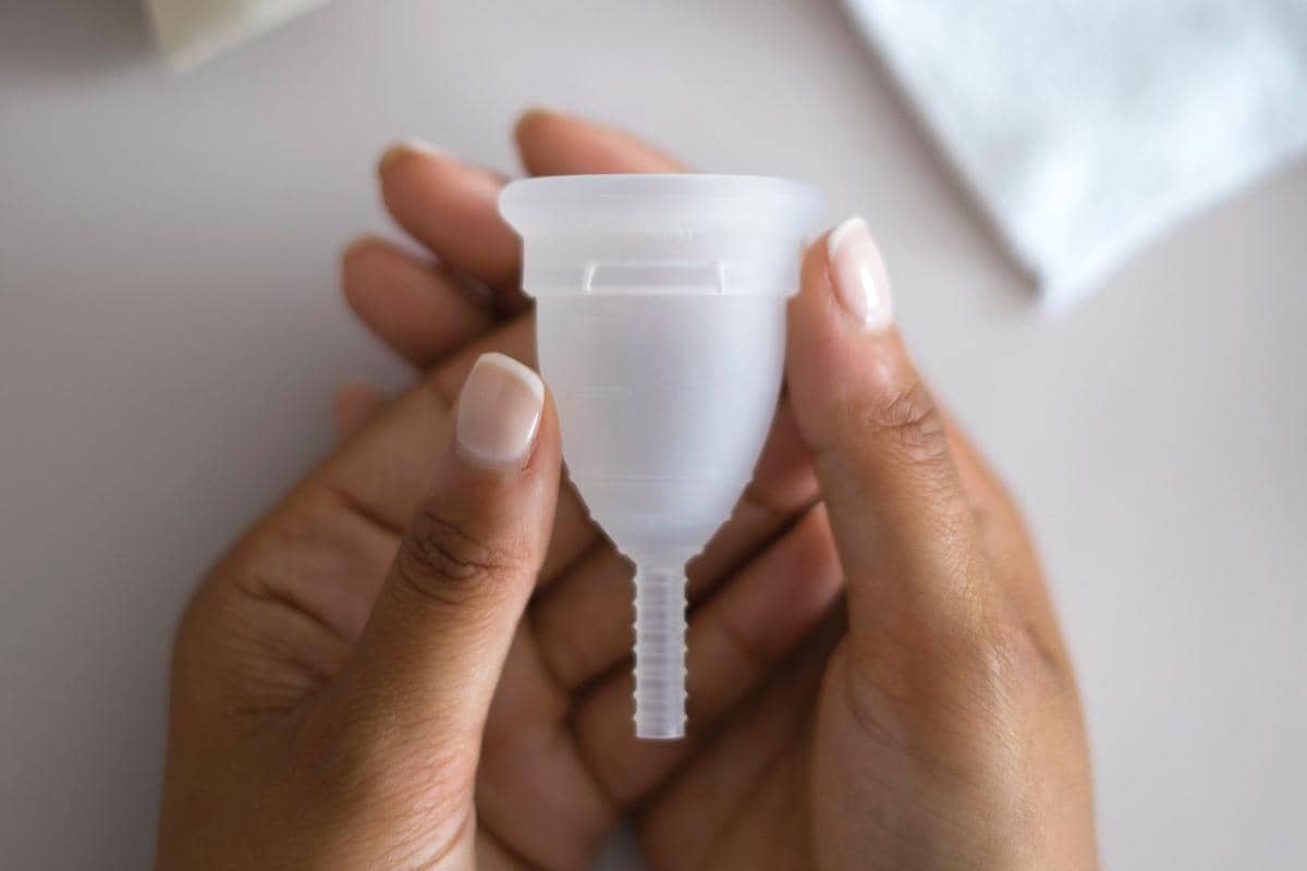 Menstrual cup berwarna merah muda diletakkan di atas kain putih sebagai ilustrasi produk kebersihan menstruasi.