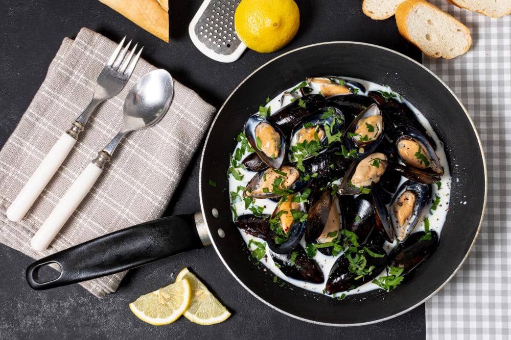 Semangkuk moules marinières berisi kerang laut hitam yang dimasak dengan kuah berbumbu dan disajikan hangat.