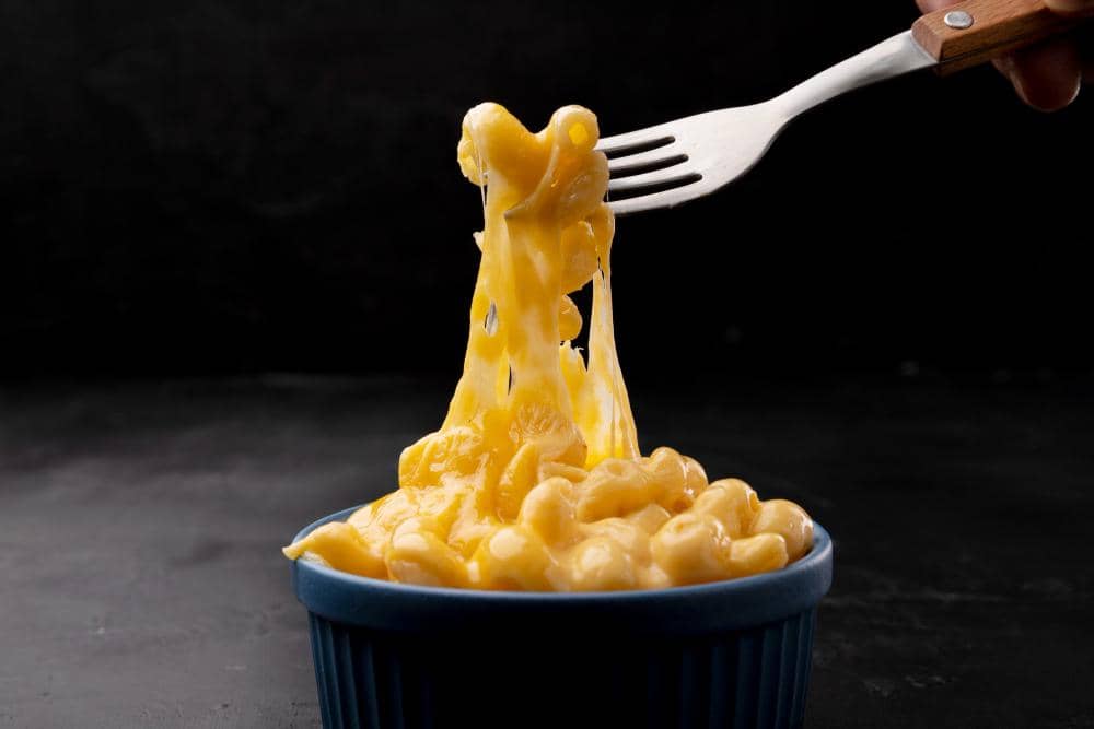 Ilustrasi semangkuk mac and cheese dengan pasta makaroni berlapis saus keju kental, disajikan hangat.