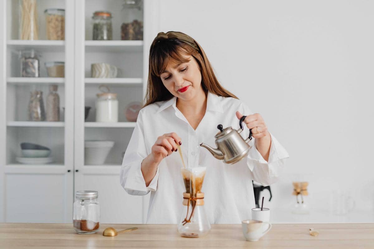 Tangan menuangkan air panas dari ketel ke penyaring kopi di atas cangkir, menggambarkan proses menyeduh kopi manual.