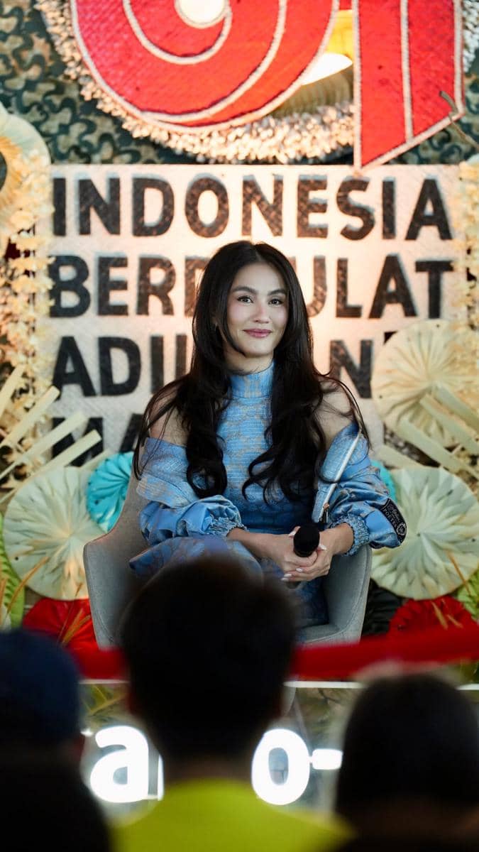 Agnez Mo berada di panggung acara Indonesia Berkarya, mengenakan busana putih sambil memegang mikrofon.