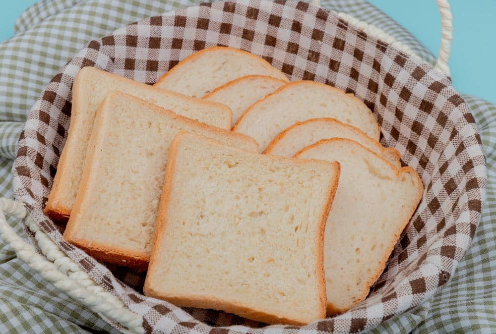 Ilustrasi beberapa lembar roti tawar berwarna cokelat muda tersusun di atas permukaan putih dengan latar belakang polos.