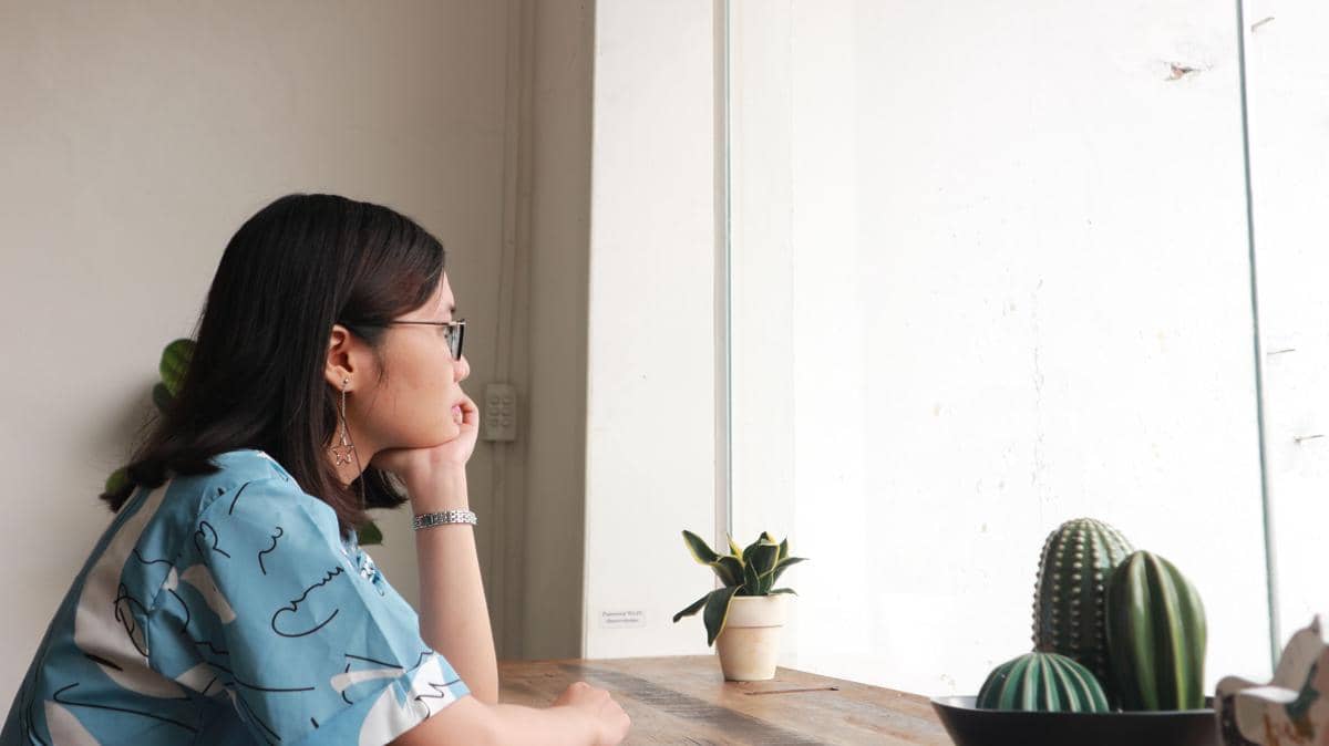 Perempuan menopang dagu sambil termenung melihat ke luar jendela.  