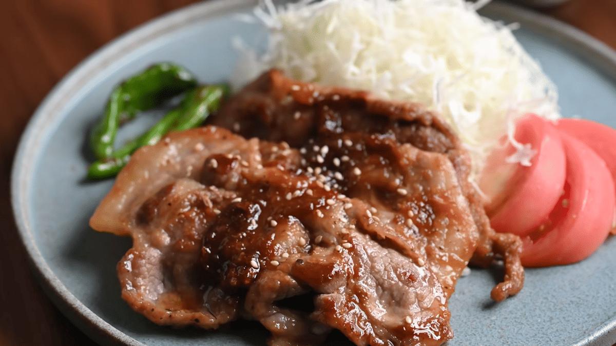 Sepiring buta shogayaki, irisan daging babi tumis jahe berlapis saus cokelat, disajikan bersama sayuran.
