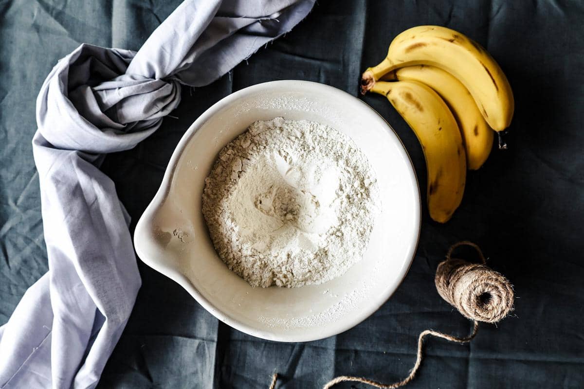 Aneka bahan untuk membuat chocolate banana bran muffin, termasuk pisang, cokelat, tepung, dan telur, tersusun di atas meja.