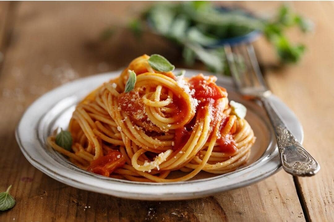 Ilustrasi sepiring spaghetti dengan saus tomat dan taburan keju, disajikan di atas meja sebagai hidangan pasta.