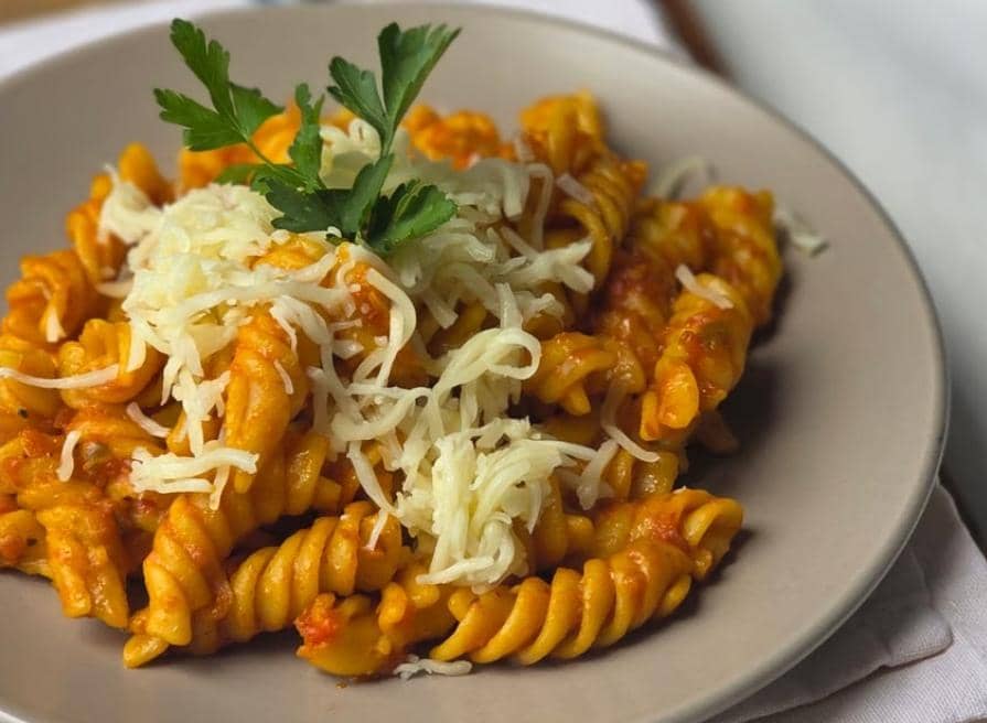 Ilustrasi pasta fusilli berwarna kuning dengan bentuk spiral, disajikan sebagai hidangan sederhana.