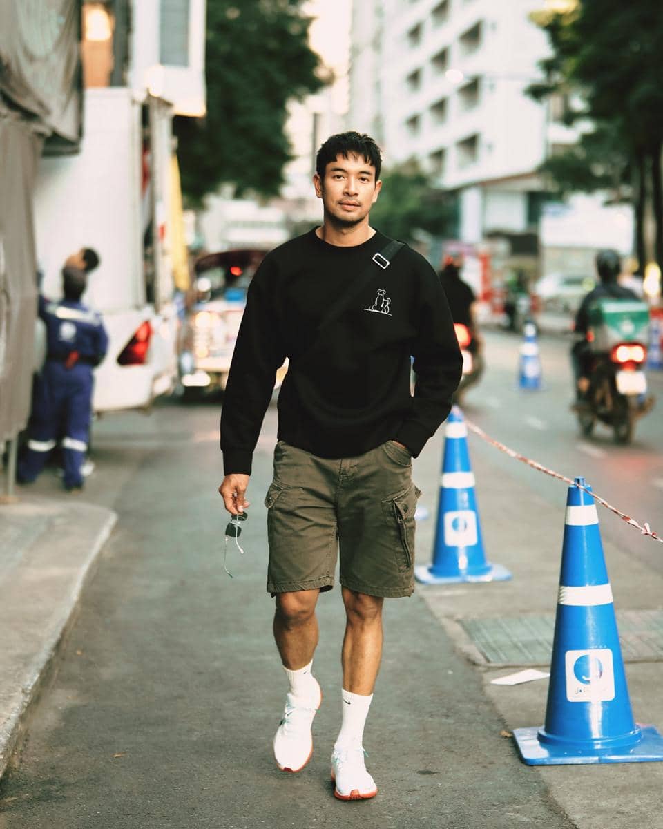 Great Warintorn mengenakan kaus putih, celana panjang hitam, dan sneakers putih dalam gaya OOTD kasual.