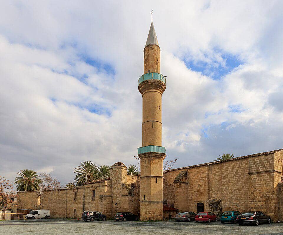 Menara batu Masjid Omeriye di Nicosia menjulang di atas bangunan beratap genteng di bawah langit cerah.