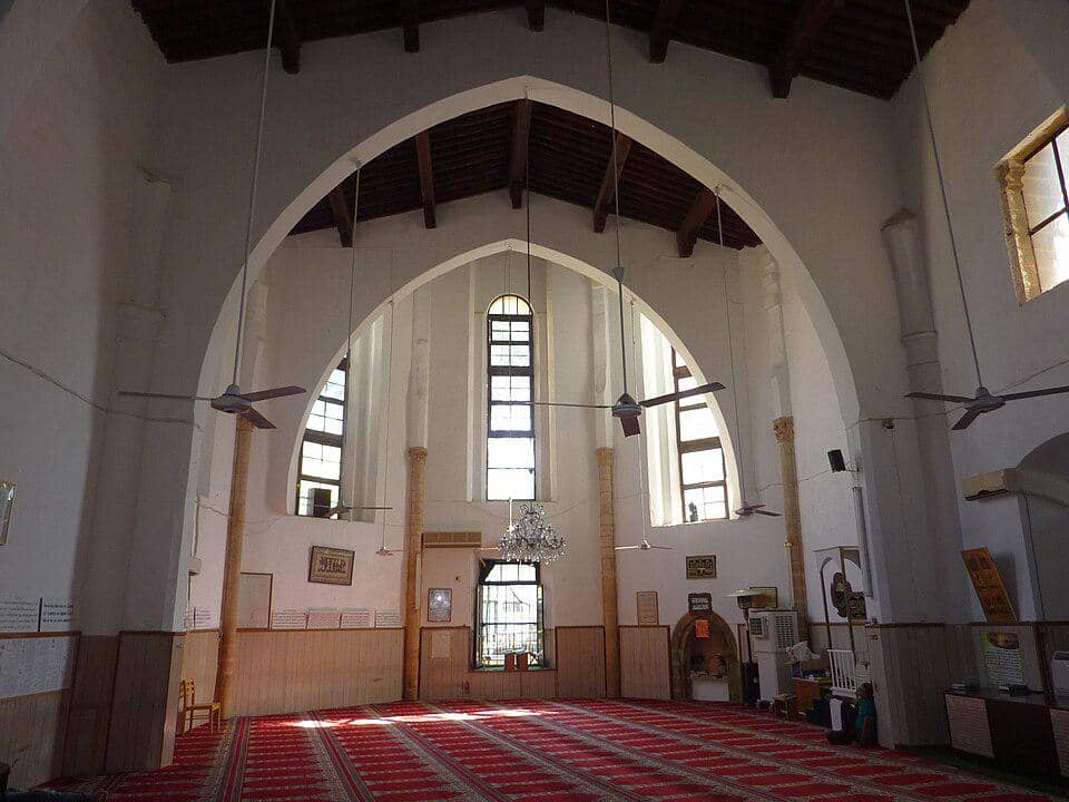Interior aula salat Masjid Omeriye di Nicosia dengan deretan lengkungan, karpet, lampu gantung, dan ornamen dinding.