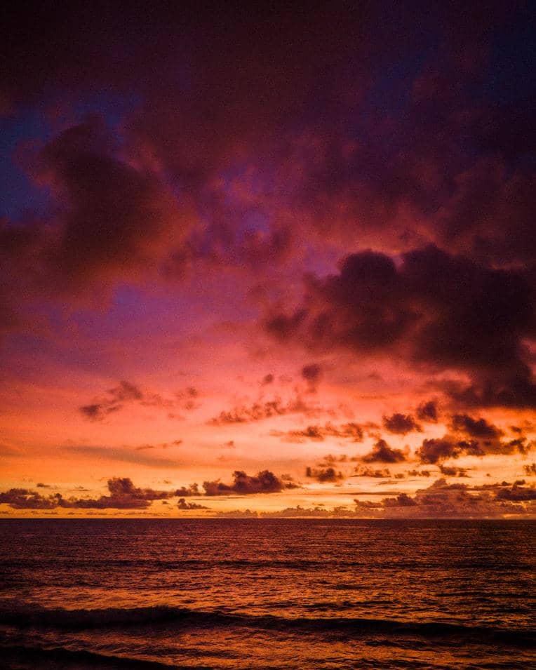 Senja berwarna oranye kemerahan di atas laut dengan awan, menggambarkan suasana matahari terbenam yang tenang.