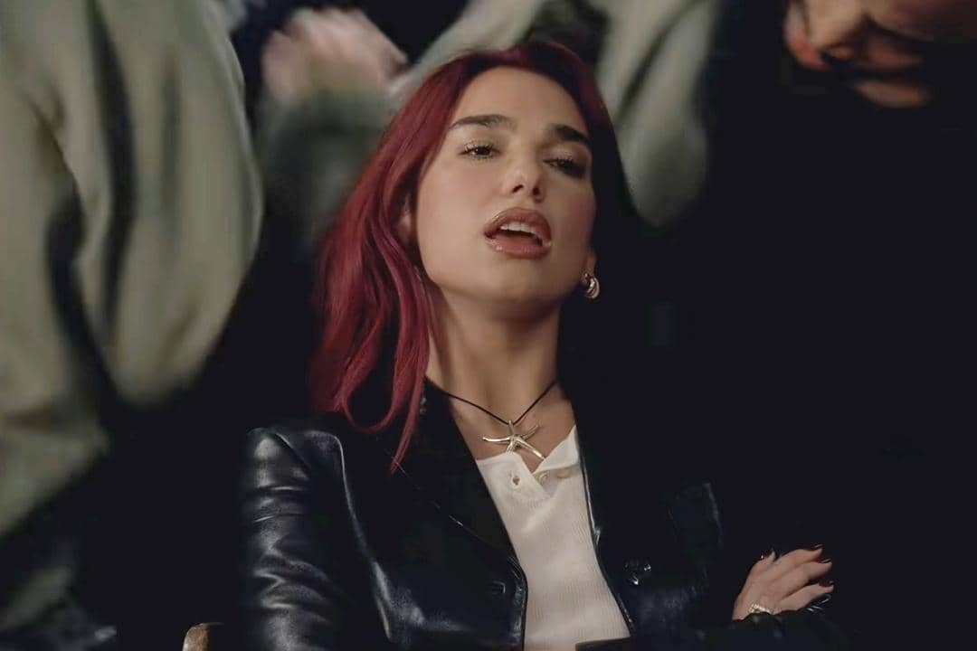 Dua Lipa tampil dalam visual musik “Training Season” dengan busana hitam dan latar ruang bergaya retro.