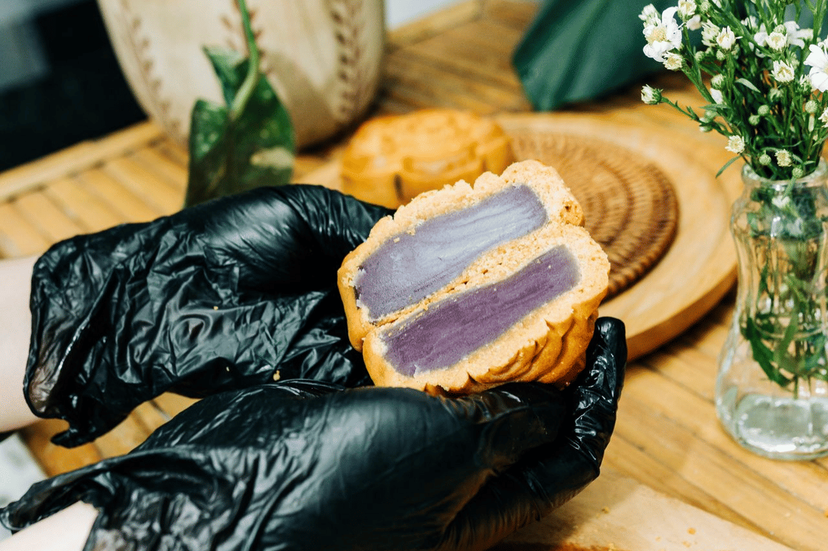 Ilustrasi isian yam berwarna ungu untuk mooncake, disajikan dalam mangkuk putih dengan sendok kayu.