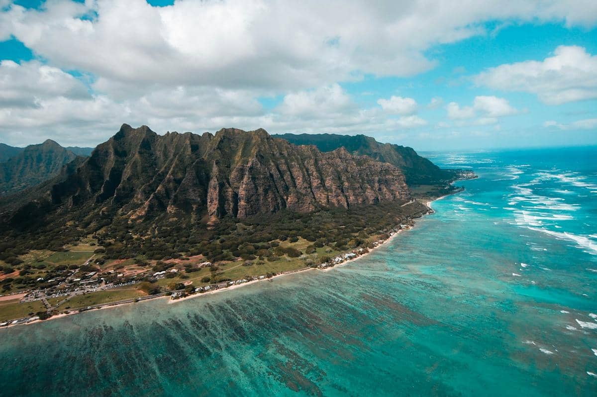 Pemandangan udara bukit hijau terjal dan garis pantai pasir putih Oahu Hawaii